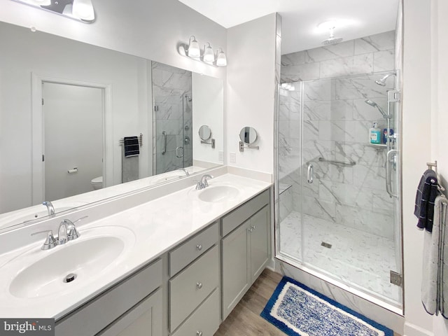 bathroom featuring toilet, a marble finish shower, a sink, and wood finished floors