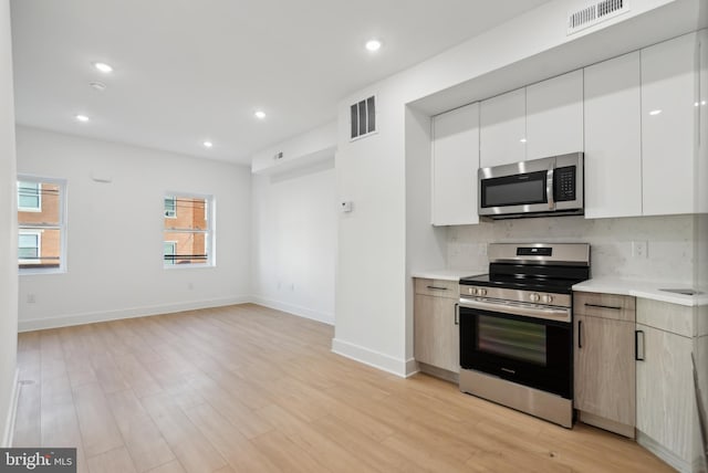 kitchen with decorative backsplash, light wood-type flooring, stainless steel appliances, and white cabinetry