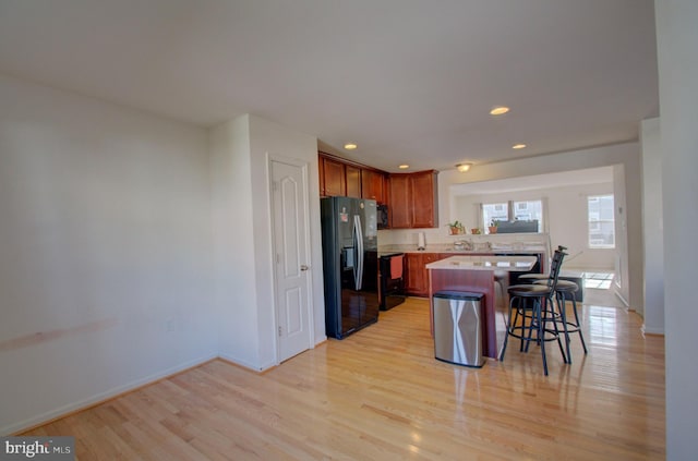 kitchen featuring light hardwood / wood-style flooring, black appliances, a center island, a kitchen bar, and kitchen peninsula