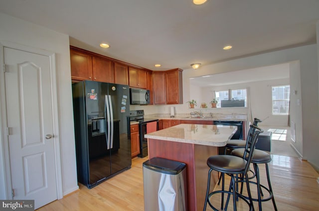 kitchen with a center island, black appliances, light hardwood / wood-style floors, sink, and a kitchen breakfast bar