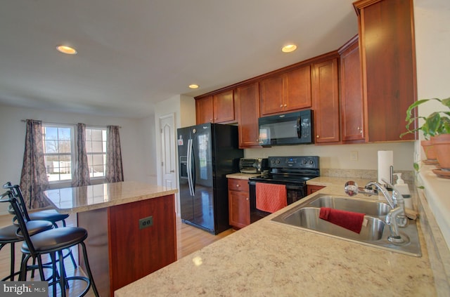 kitchen with light hardwood / wood-style flooring, a breakfast bar area, black appliances, sink, and kitchen peninsula