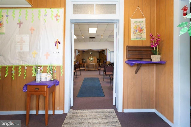 hall featuring a drop ceiling and wood walls