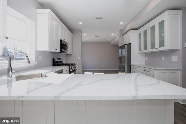 kitchen with visible vents, white cabinets, glass insert cabinets, stainless steel appliances, and a sink