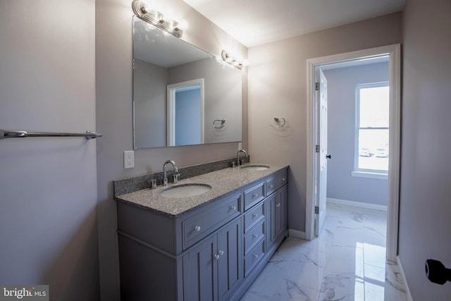 bathroom with marble finish floor, double vanity, a sink, and baseboards