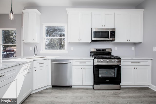 kitchen featuring stainless steel appliances, white cabinetry, a sink, and light wood finished floors