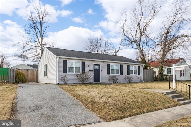 ranch-style home with aphalt driveway, roof with shingles, fence, and a front lawn