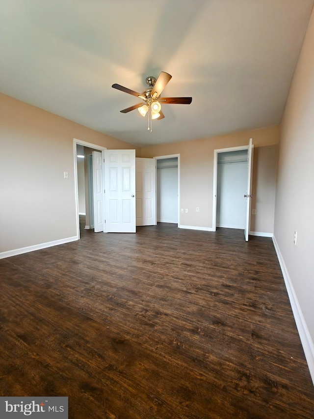 unfurnished bedroom featuring multiple closets, dark wood-type flooring, and ceiling fan