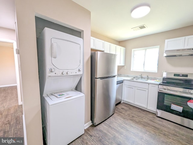 kitchen with stacked washer and dryer, appliances with stainless steel finishes, sink, and white cabinets