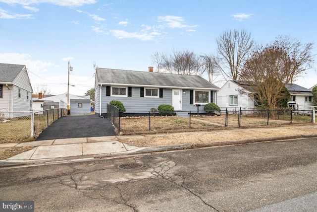 ranch-style house featuring driveway, a fenced front yard, a chimney, and an outbuilding