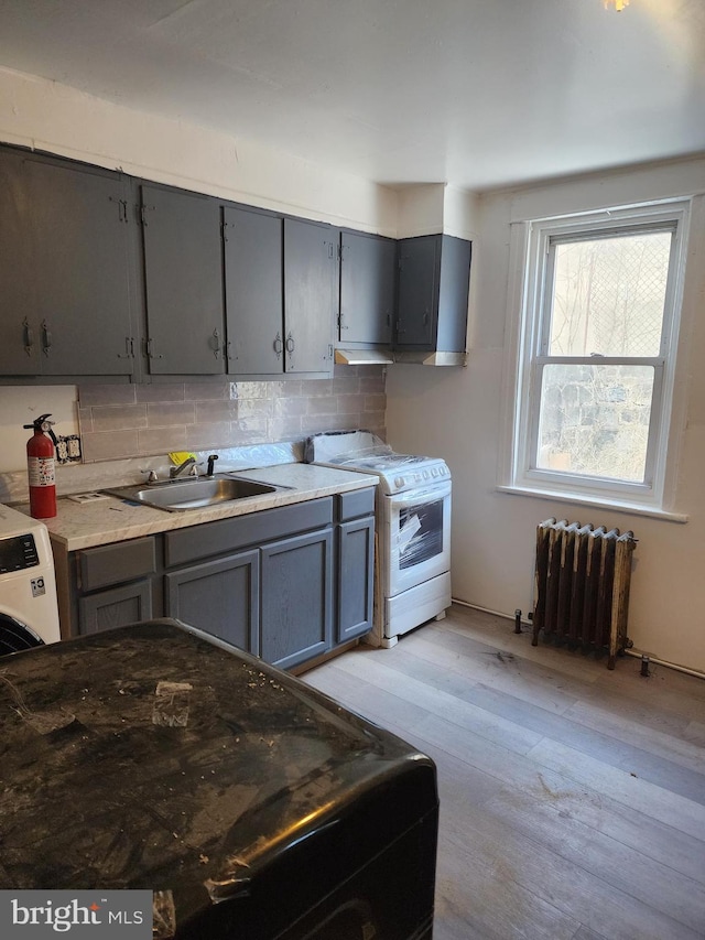 kitchen with light wood-type flooring, white gas stove, gray cabinets, a sink, and radiator heating unit