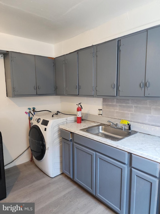 clothes washing area featuring cabinet space, washer / clothes dryer, light wood-type flooring, and a sink