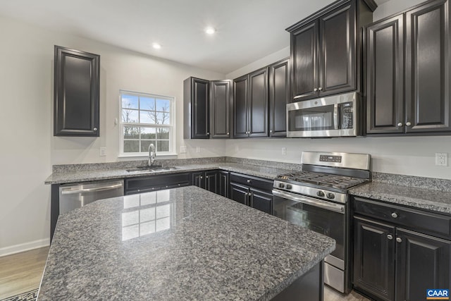 kitchen featuring sink, a center island, light wood-type flooring, appliances with stainless steel finishes, and dark stone counters