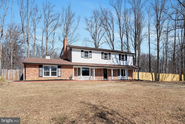 traditional-style house featuring a front yard, a chimney, fence, and brick siding