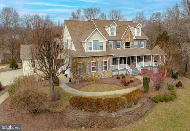 view of front of property with covered porch, stone siding, and concrete driveway