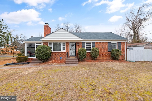 view of front of home with brick siding, a chimney, a front yard, a sunroom, and fence