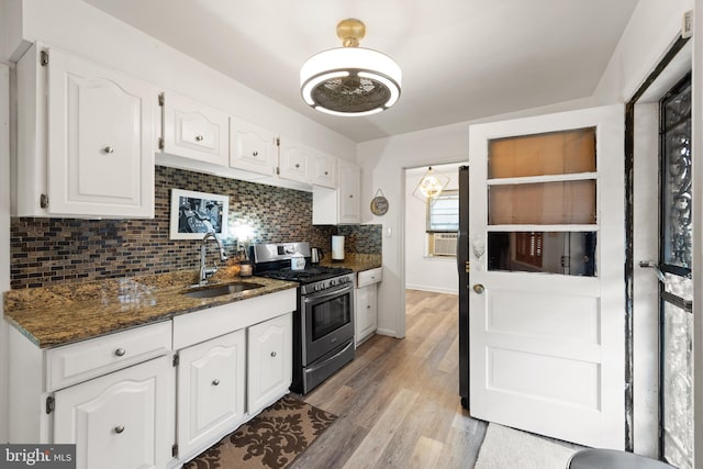 kitchen with white cabinets, backsplash, dark stone countertops, stainless steel range with gas cooktop, and a sink