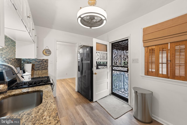 kitchen with light stone counters, a sink, white cabinets, fridge with ice dispenser, and decorative backsplash