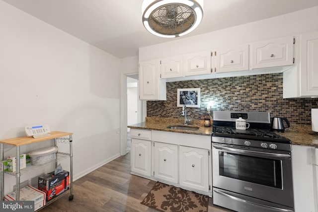 kitchen with dark stone counters, white cabinets, a sink, backsplash, and gas stove