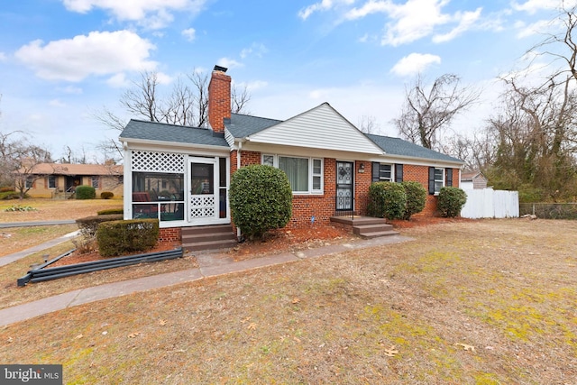 view of front of property featuring a shingled roof, a sunroom, a chimney, fence, and brick siding