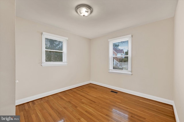 empty room featuring hardwood / wood-style floors, visible vents, and baseboards