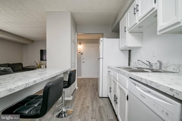 kitchen with white appliances, white cabinets, light wood-style flooring, light countertops, and a sink