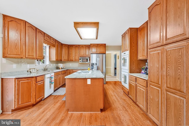 kitchen with stainless steel appliances, a sink, a center island, light wood-style floors, and brown cabinets