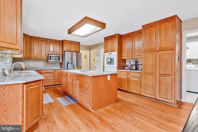 kitchen with washer / dryer, a kitchen island, stainless steel appliances, light wood-style floors, and a sink