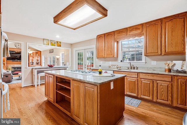 kitchen with french doors, white gas cooktop, light wood-style floors, a kitchen island, and a sink