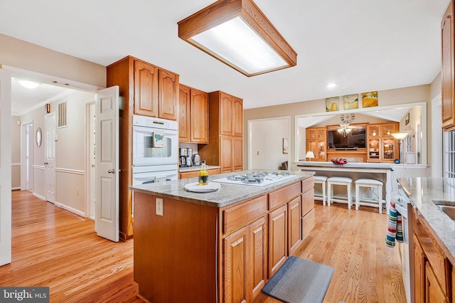 kitchen with white appliances, a kitchen island, light wood finished floors, and light stone countertops