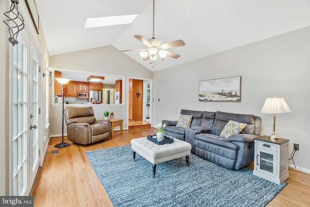 living room featuring visible vents, light wood-style flooring, lofted ceiling with skylight, a ceiling fan, and baseboards