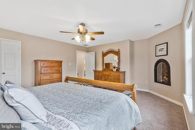 carpeted bedroom with a warm lit fireplace, ceiling fan, visible vents, and baseboards