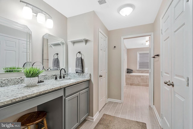 bathroom with tiled tub, vanity, visible vents, and baseboards