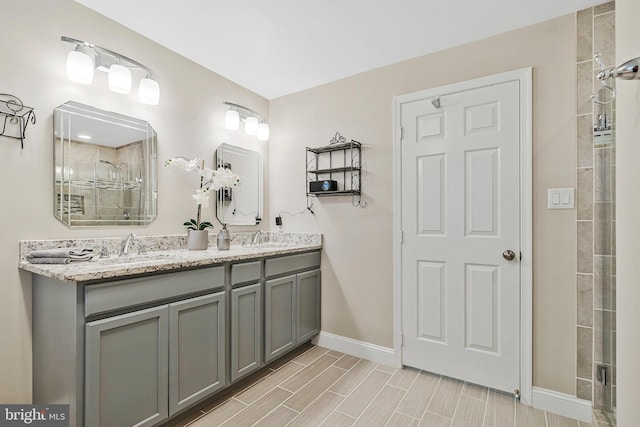 full bath featuring double vanity, baseboards, a tile shower, and a sink