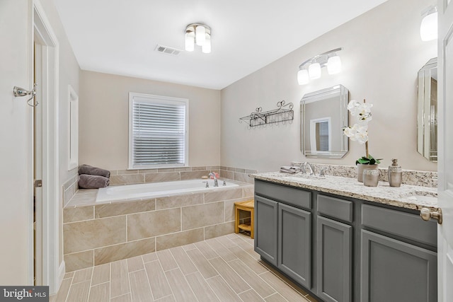 full bath featuring a bath, double vanity, a sink, and visible vents