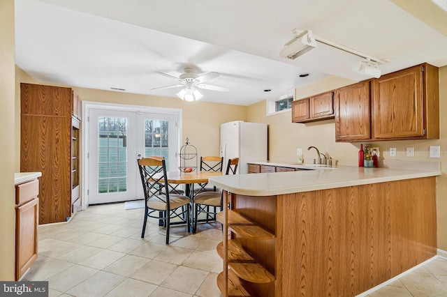 kitchen with white refrigerator with ice dispenser, brown cabinetry, a peninsula, light countertops, and open shelves