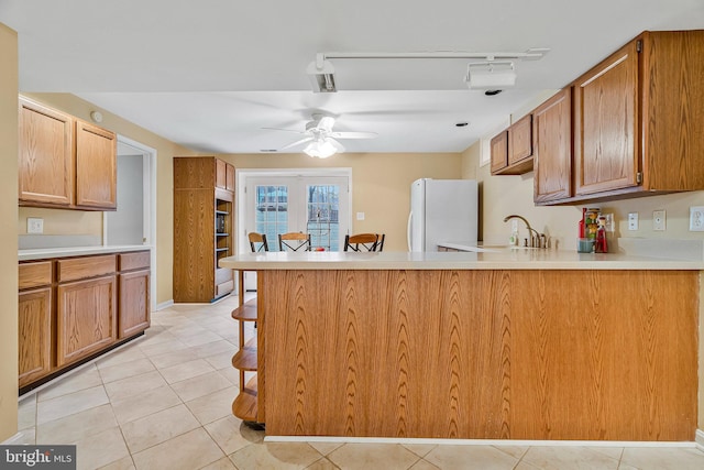 kitchen with ceiling fan, a breakfast bar area, freestanding refrigerator, a peninsula, and light countertops