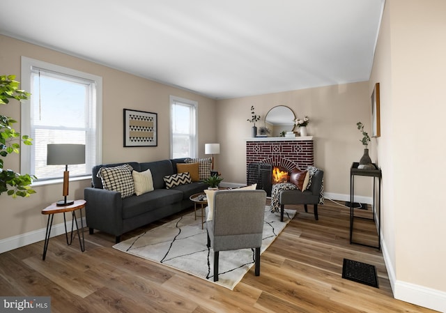 living room featuring light wood-type flooring, a brick fireplace, baseboards, and visible vents