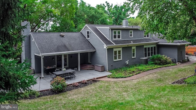 rear view of property with a shingled roof, stucco siding, a chimney, a patio area, and a lawn