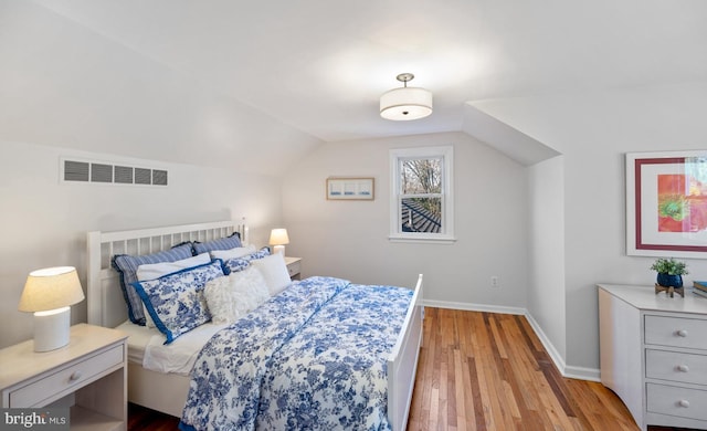 bedroom featuring visible vents, lofted ceiling, baseboards, and wood finished floors