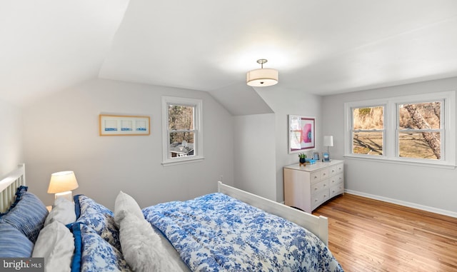bedroom with lofted ceiling, light wood-style floors, and baseboards