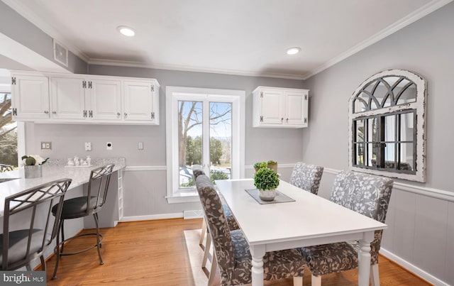 dining room featuring a wainscoted wall, recessed lighting, crown molding, and light wood-style floors
