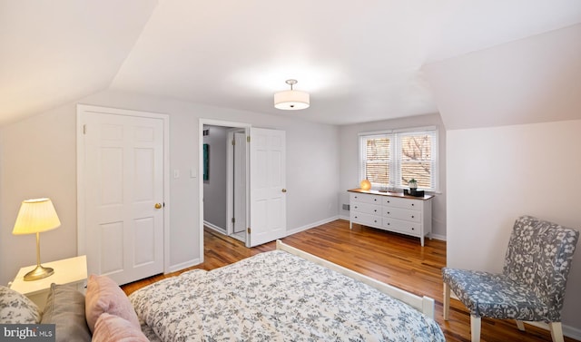 bedroom with vaulted ceiling, baseboards, and wood finished floors