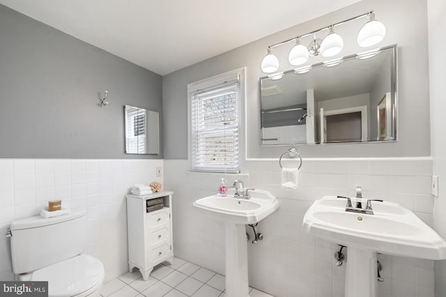 bathroom featuring tile patterned floors, a wainscoted wall, toilet, and tile walls