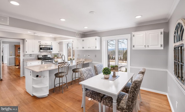 dining room with crown molding, recessed lighting, light wood-style floors, and a wainscoted wall