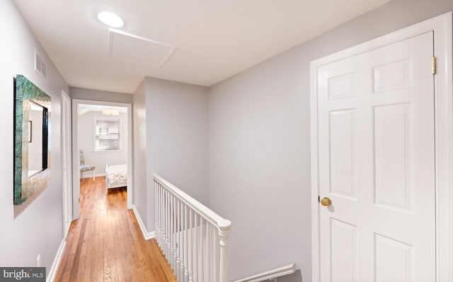 hall with an upstairs landing, visible vents, light wood-type flooring, and baseboards