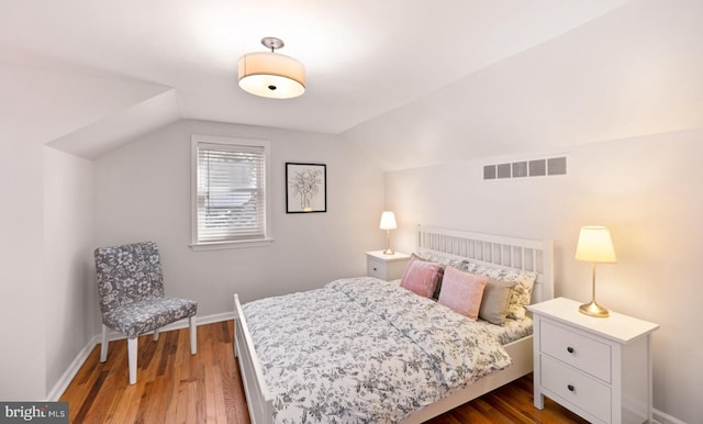 bedroom featuring visible vents, baseboards, wood finished floors, and vaulted ceiling