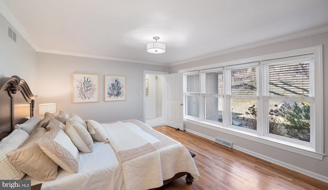 bedroom with crown molding, wood finished floors, visible vents, and baseboards