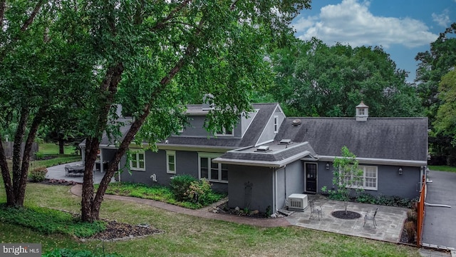 rear view of property with stucco siding, an outdoor fire pit, a yard, a shingled roof, and a patio area