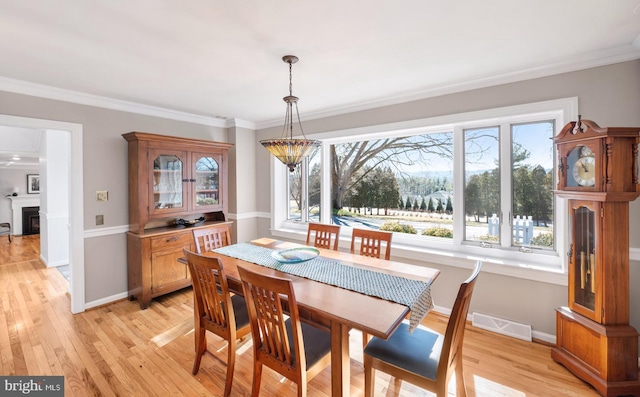 dining room featuring visible vents, light wood-style flooring, a fireplace, crown molding, and baseboards