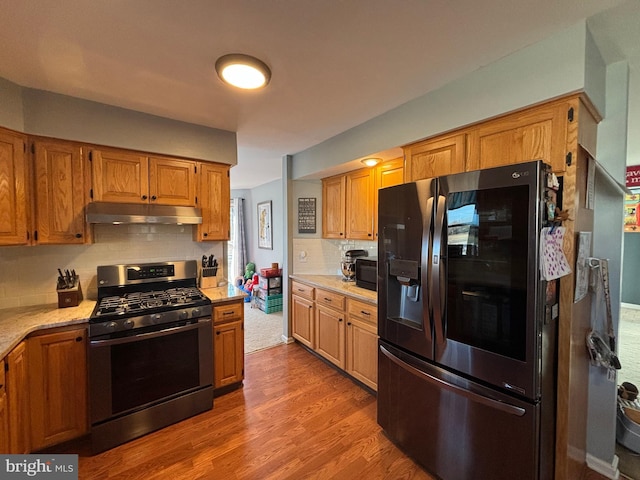 kitchen featuring tasteful backsplash, appliances with stainless steel finishes, hardwood / wood-style flooring, and light stone counters